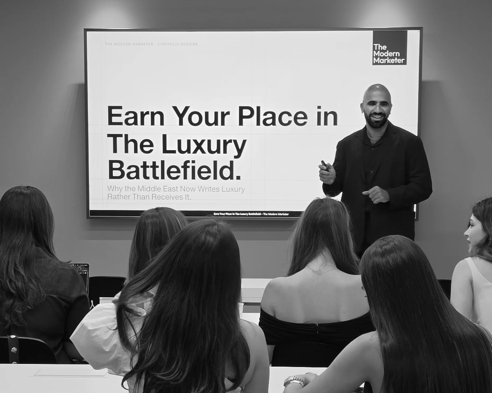 Ahmed El-Gamal smiling beside a screen that reads Earn Your Place in The Luxury Battlefield, with The Modern Marketer mark in the corner