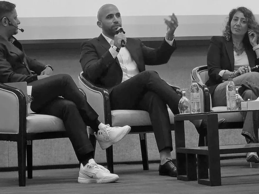 Ahmed El-Gamal speaking with a microphone on a panel, seated between two other panelists
