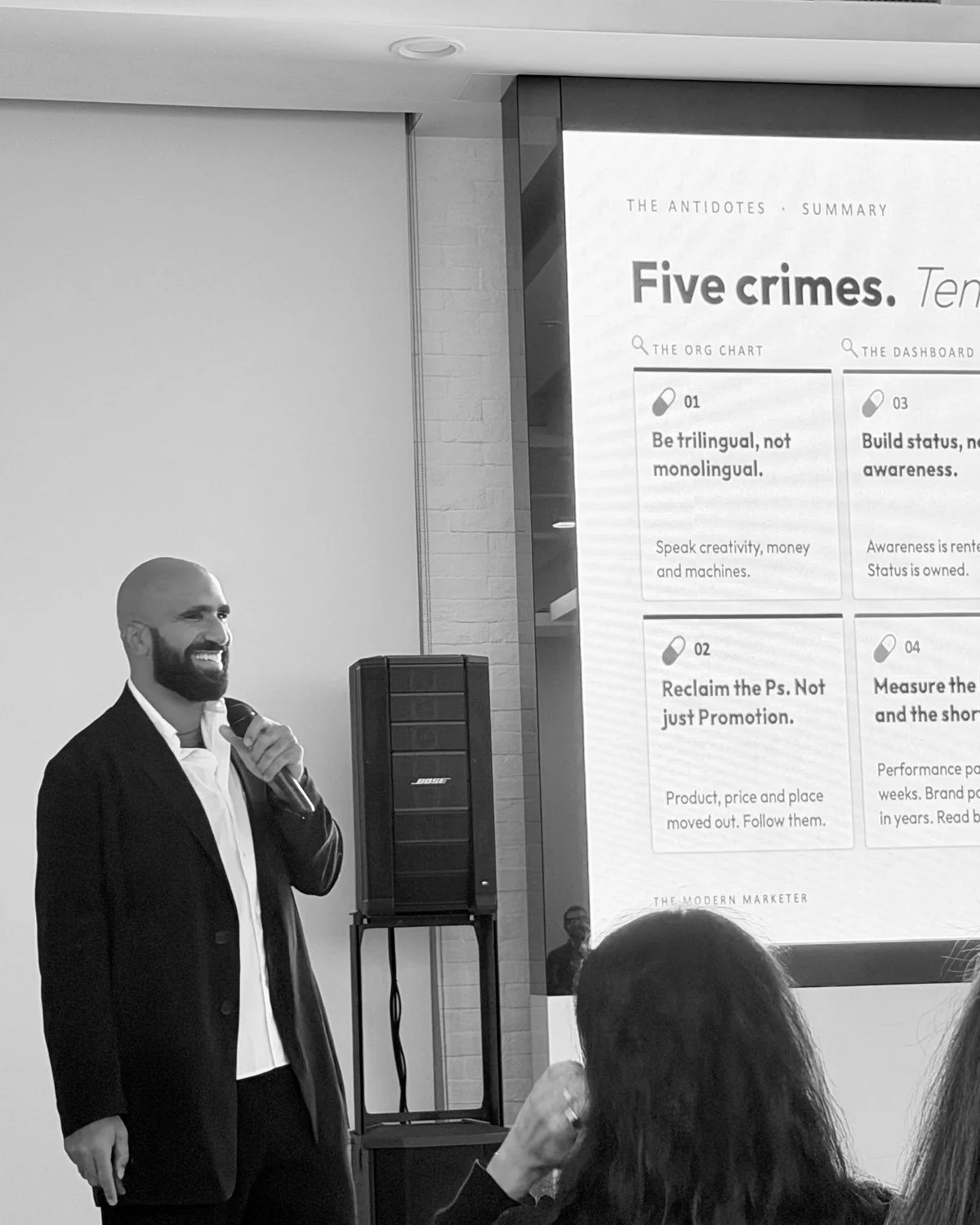 Ahmed El-Gamal smiling with a microphone beside a slide titled Five crimes