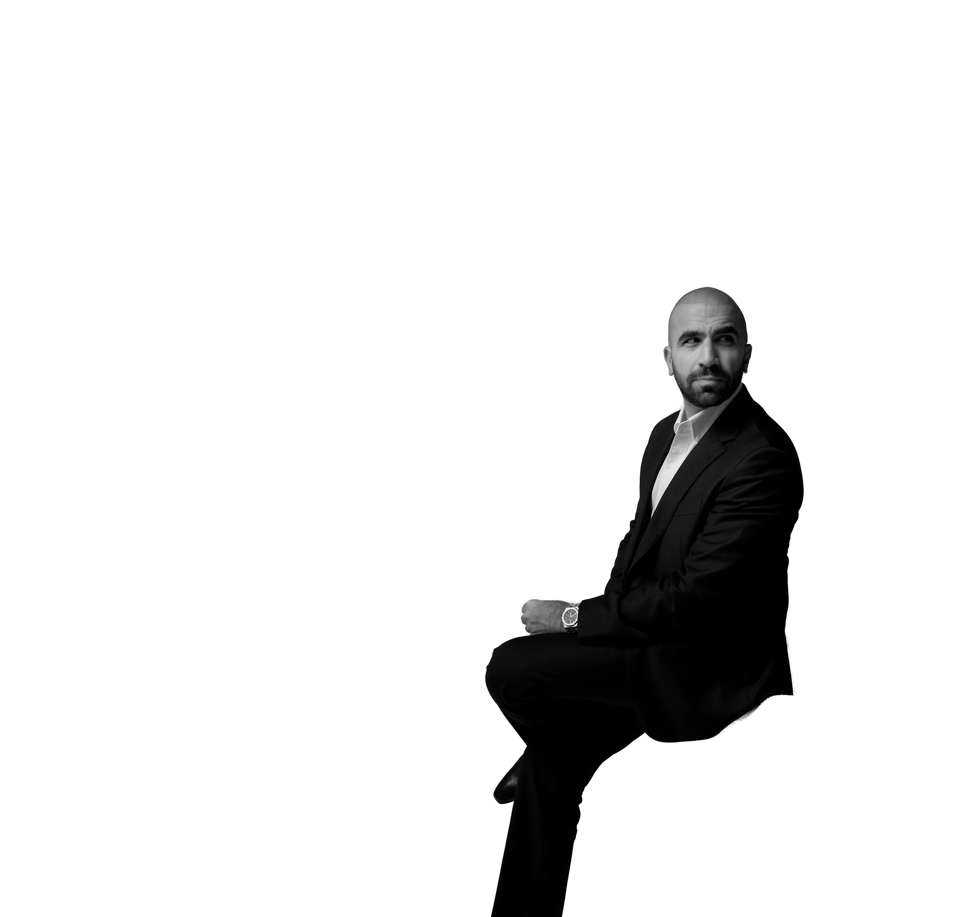 Ahmed El-Gamal seated on a white chair, looking over his shoulder, in a dark suit and white shirt
